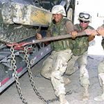 Cheater pipe being used by three military members to close a chain lock on a buldozer transporter.